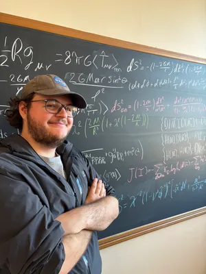 Dennis in front of a chalkboard covered with equations.